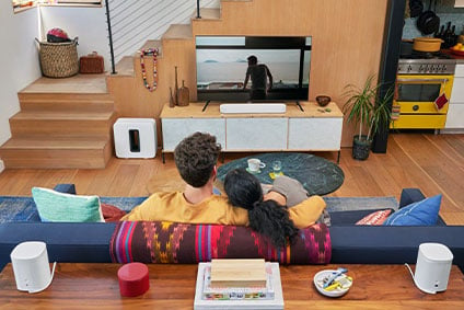 Sonos soundbar in a living room with two people enjoying a Sonos home theater setup with rear surrounds and Sonos wireless sub in their living room.