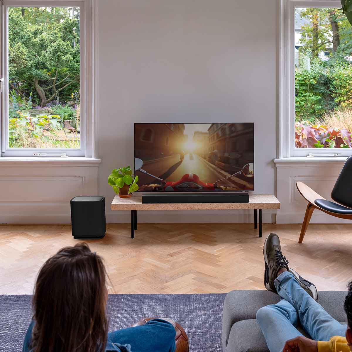 Harman Kardon Enchant Wireless Subwoofer lifestyle view couple watching tv with sub on floor to left