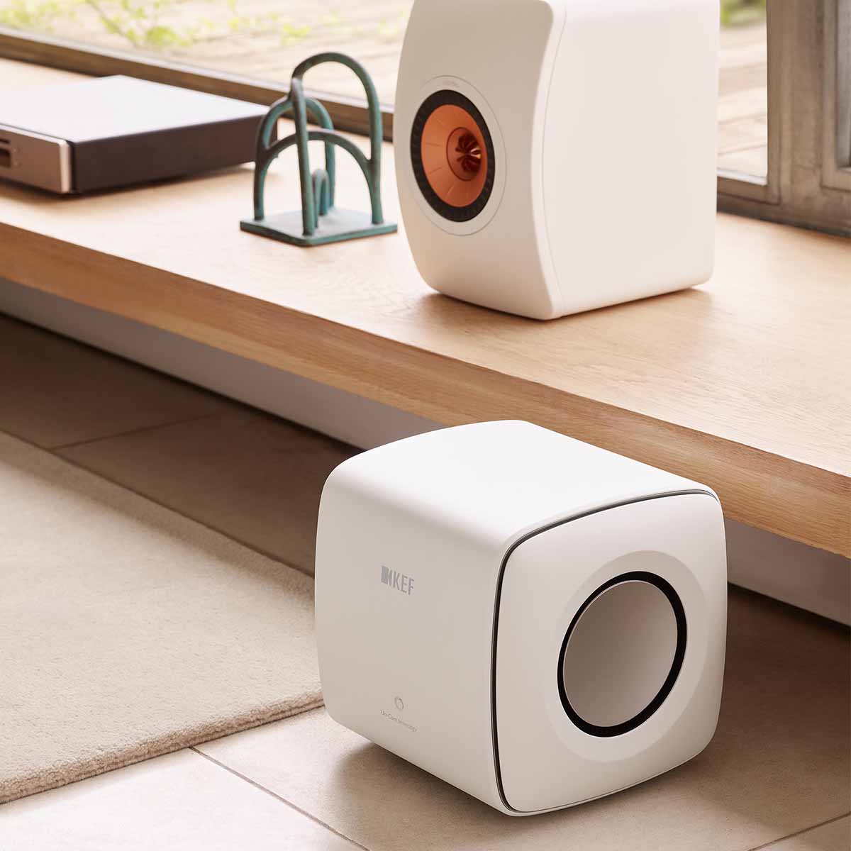 KEF KC62 Subwoofer - Mineral White - sitting on floor with LS50 speaker on shelf above