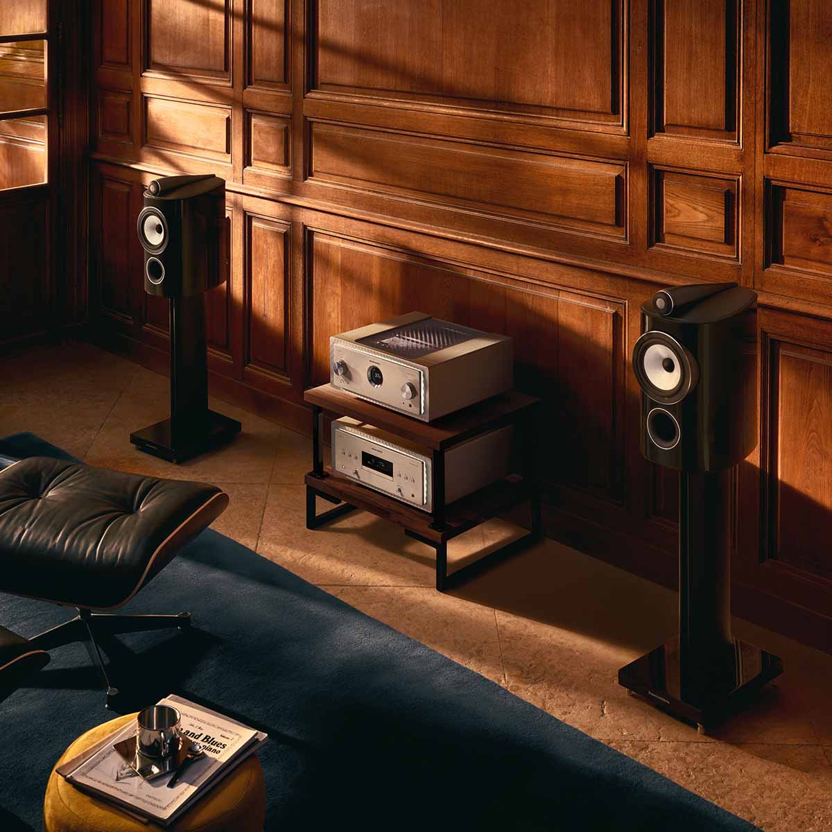 Bowers & Wilkins 805 D5 Bookshelf Loudspeaker - lifestyle photo of pair of Stealth Black speakers on stand without grille facing left with hifi system in between