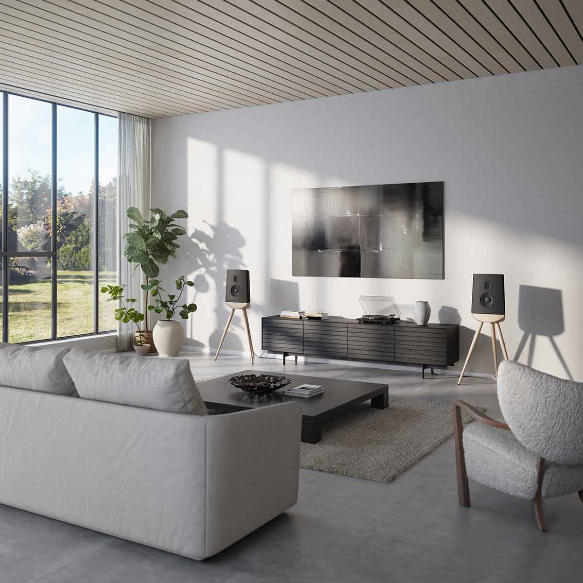 Lyngdorf Cue-100 Speaker lifestyle photo of speakers in living room, pair of black speakers with oak base and no grilles