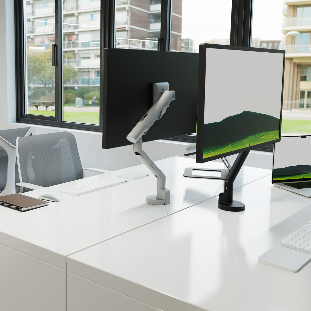 Modern office setup with two computer monitors on a desk, large windows showing an urban view.