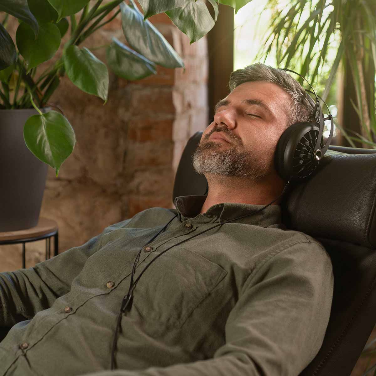 Meze 105 AER Open-Back Headphones - black lifestyle shot three-quarter view man wearing headphones reclining in a chair with eyes closed