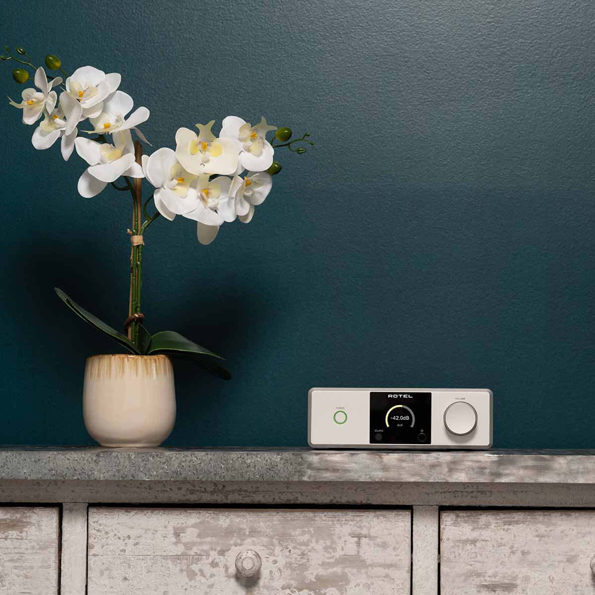 Lifestyle photo Rotel DX-5 Integrated Amplifier - silver front view on cabinet to right of white flowers in vase