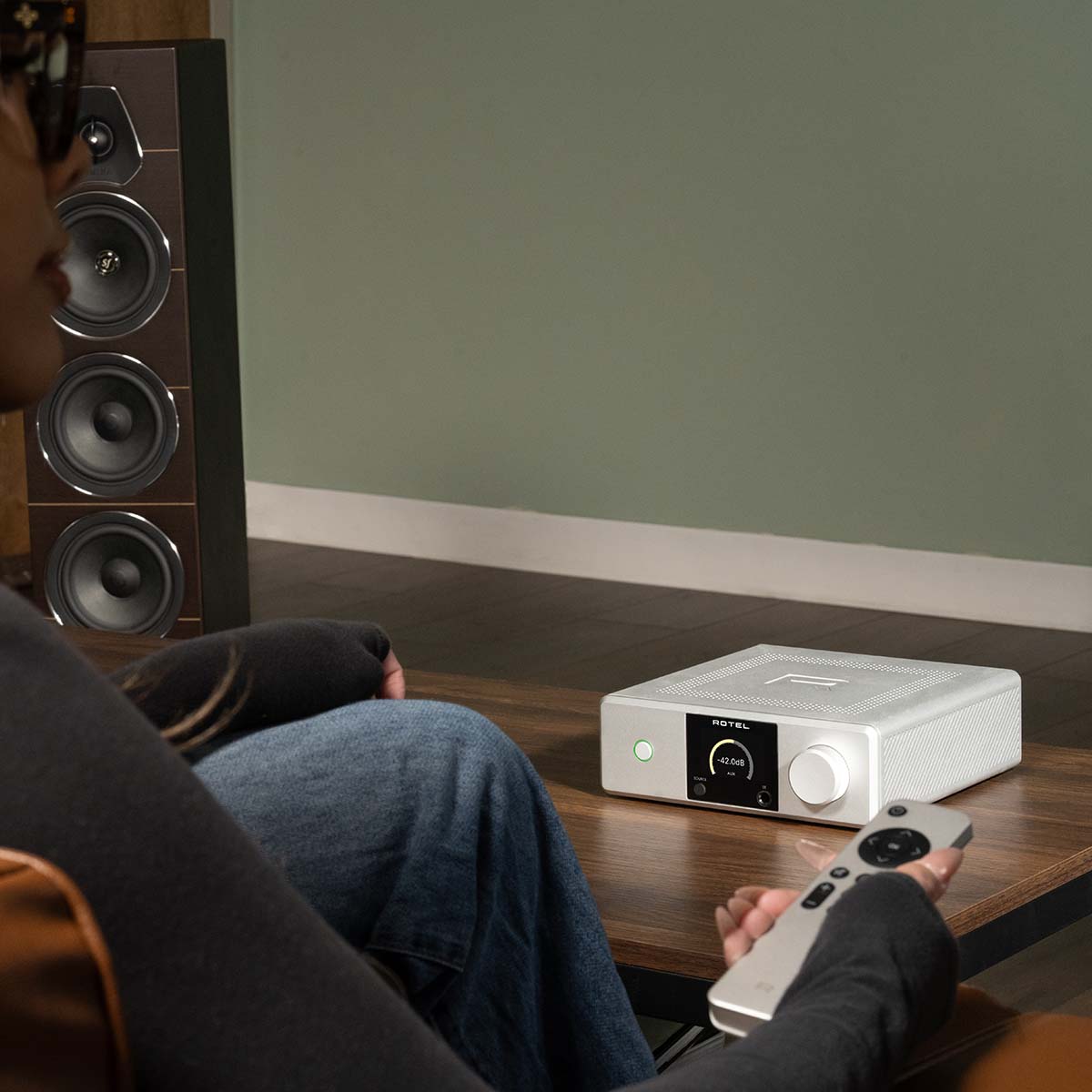 Lifestyle photo Rotel DX-5 Integrated Amplifier - silver on coffee table with person holding remote in foreground