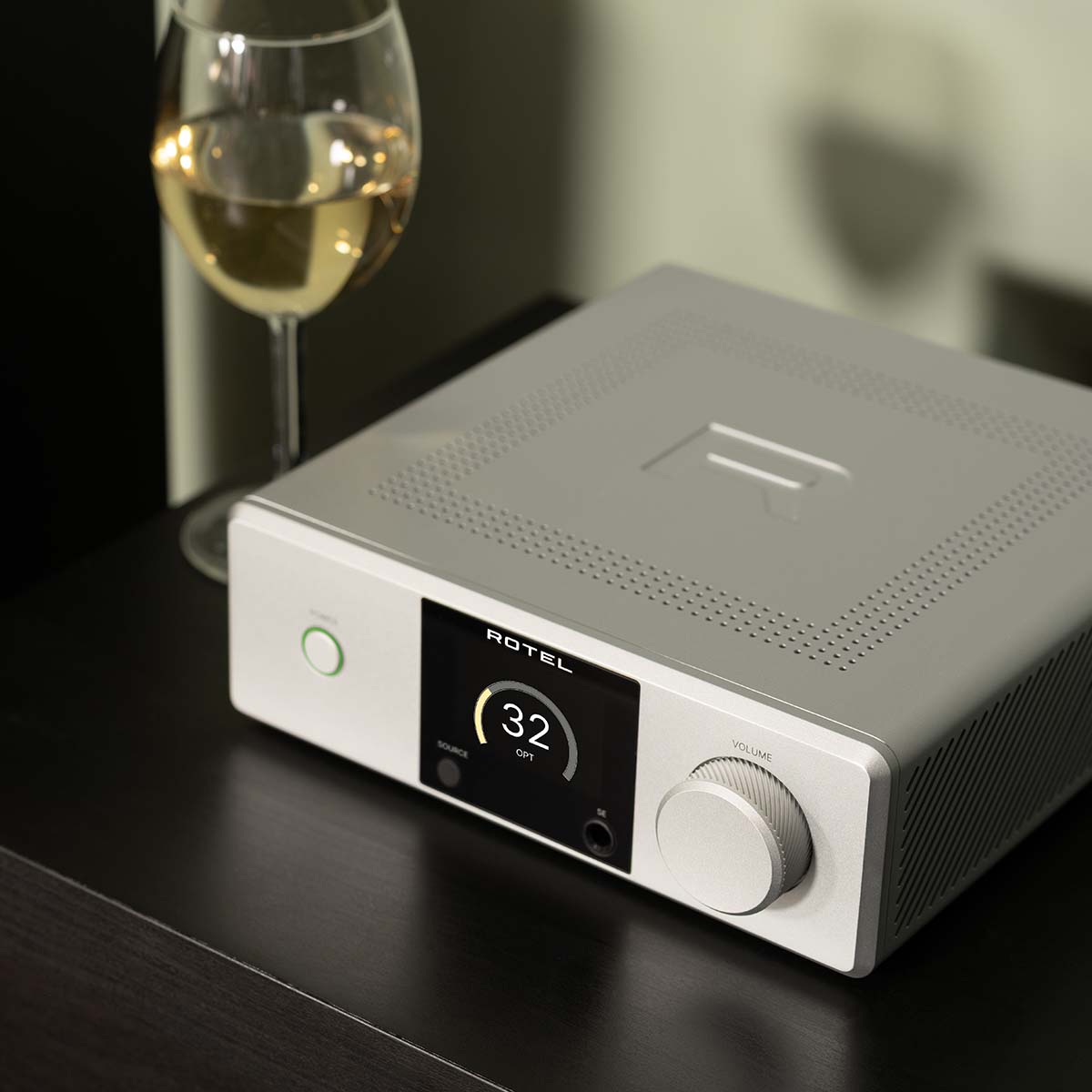Lifestyle photo Rotel DX-5 Integrated Amplifier - silver top view angled left on cabinet with wine glass in background