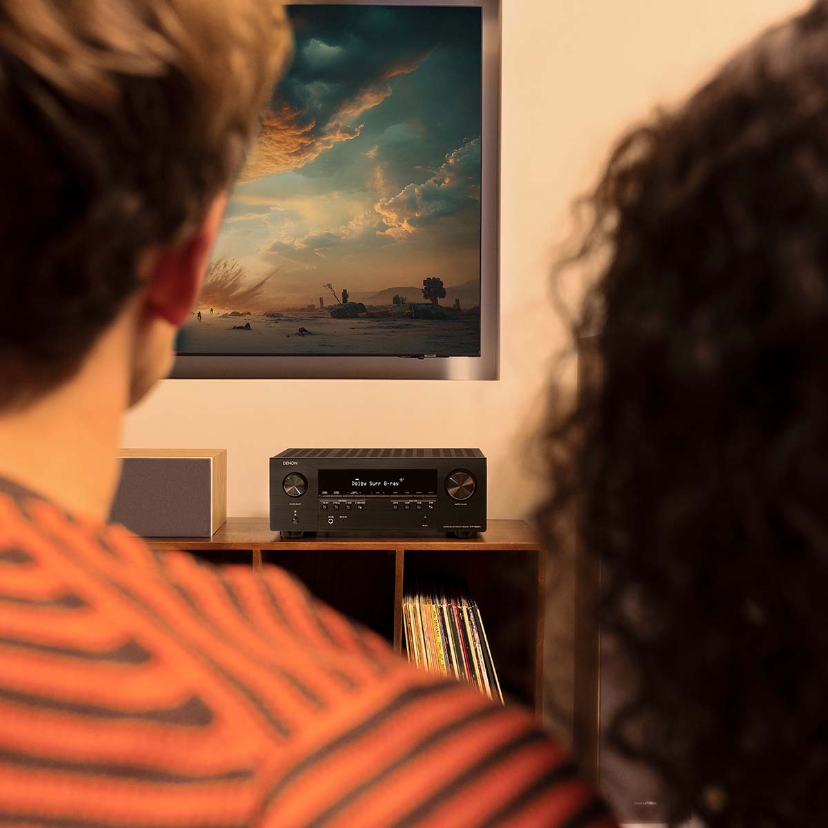 Denon AVR-S980H AV Receiver lifestyle photo of unit on cabinet with two people watching a movie in foreground