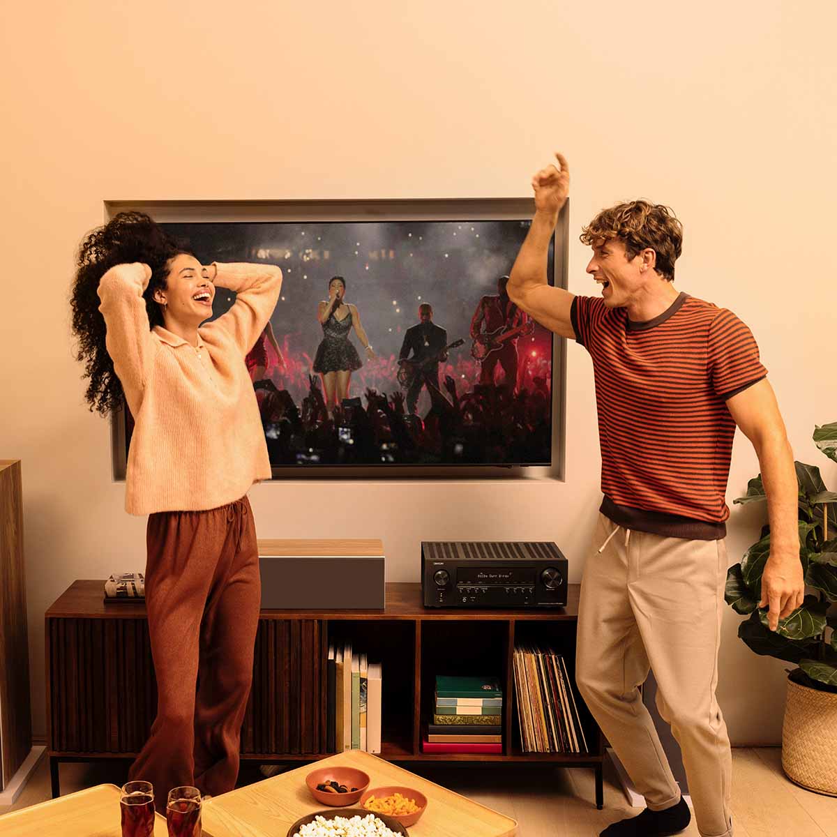 Denon AVR-S980H AV Receiver lifestyle photo of unit on cabinet with two people dancing in front of unit and tv