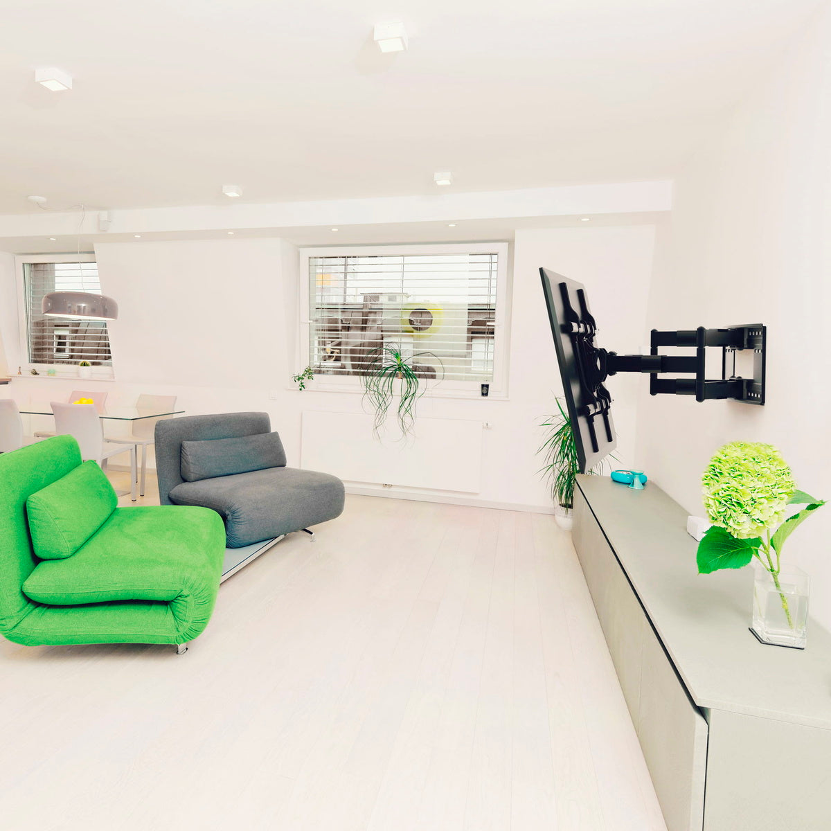 Modern living room with green sofa, gray armchair, and a TV on a white wall.