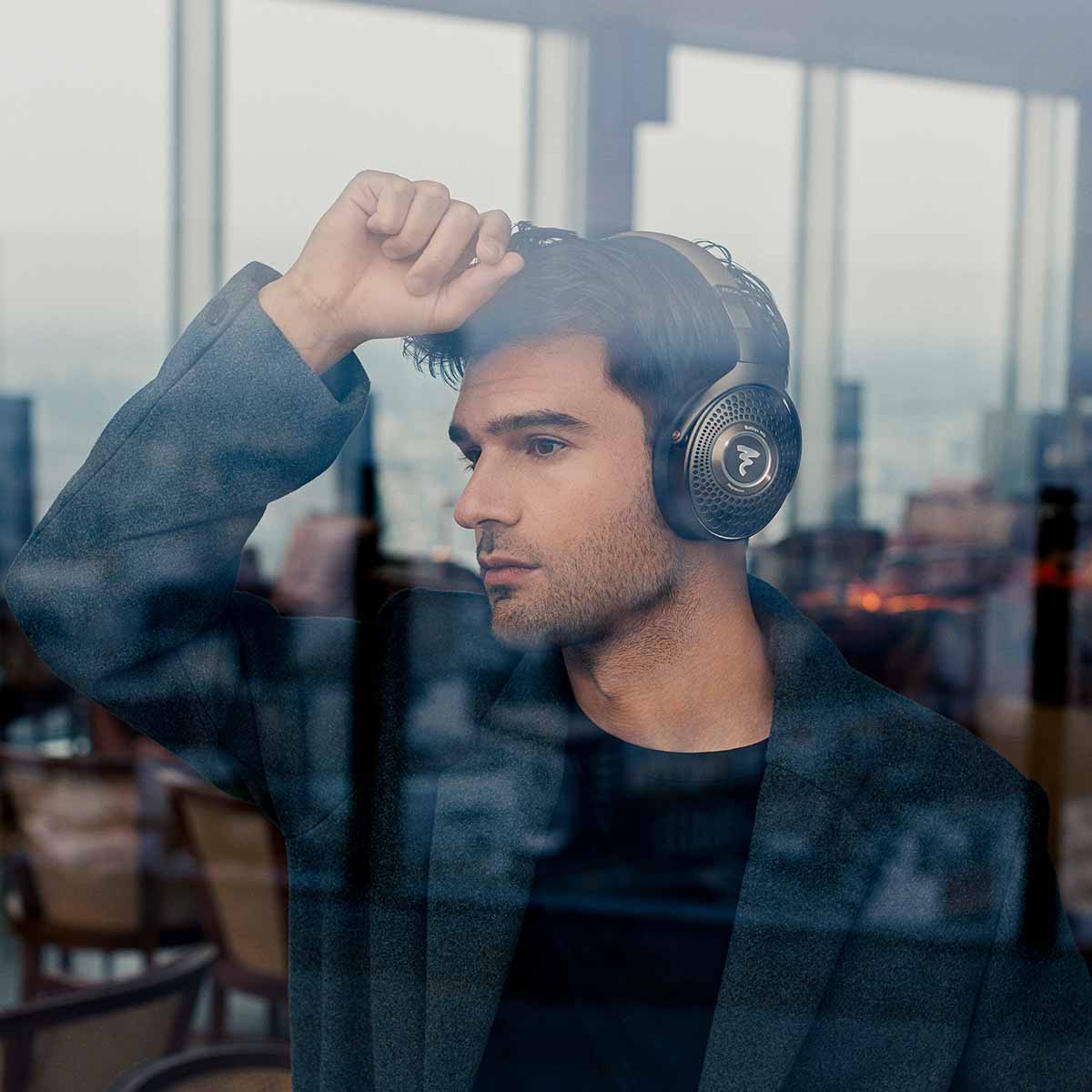 Focal Bathys MG Wireless Over-Ear Active Noise Cancelling Headphones - lifestyle shot man wearing headphones leaning on window