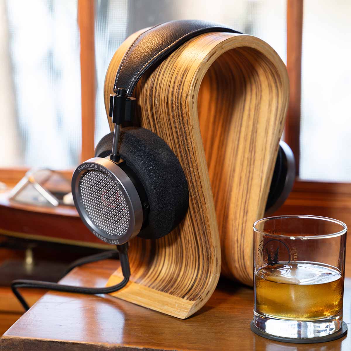 Grado Signature HP100 SE Headphones lifestyle shot three-quarter view angled right on wooden stand with whisky glass