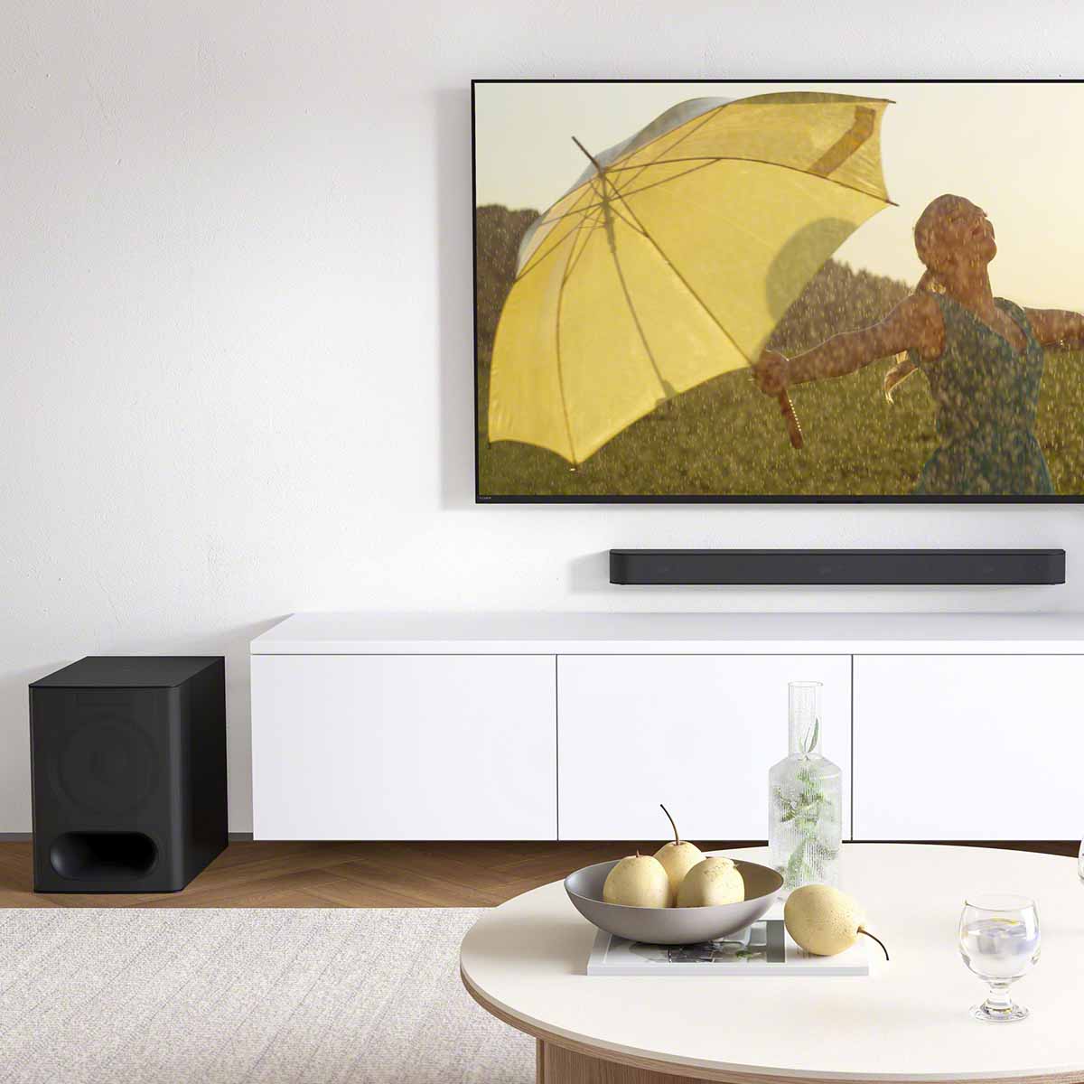 Lifestyle shot of Sony HT-S60 BRAVIA Theater System 6 5.1ch Wireless Speaker System with Subwoofer - soundbar wall-mounted underneath TV and subwoofer on ground to left