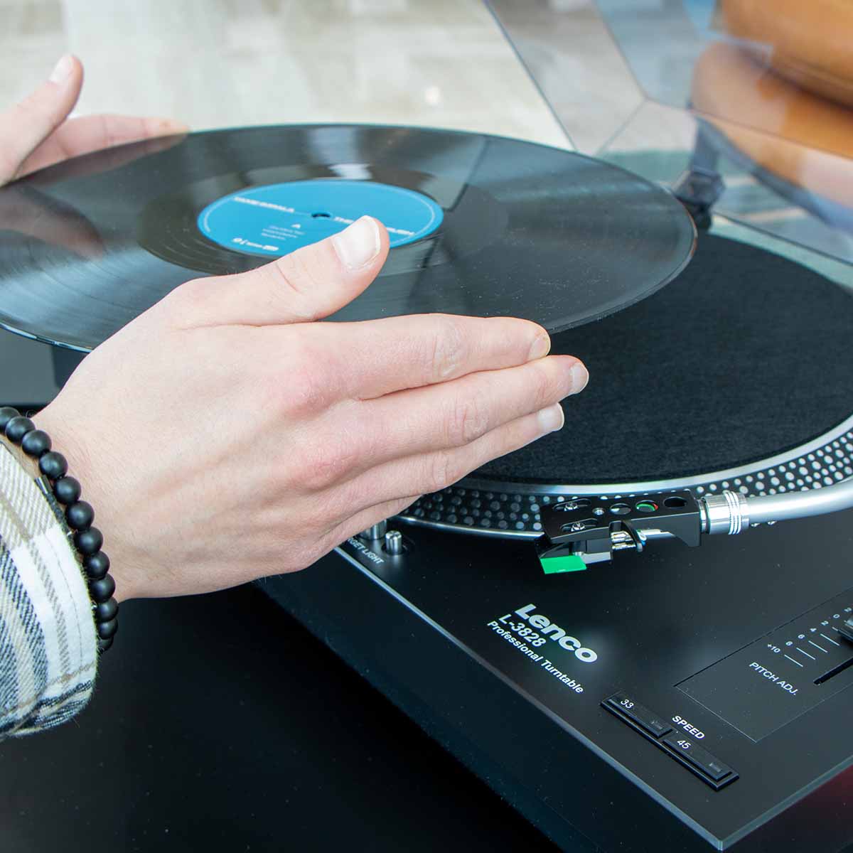 Lenco L-3828 Direct Drive Turntable high angle side view lifestyle shot of unit facing left with hands placing record on platter