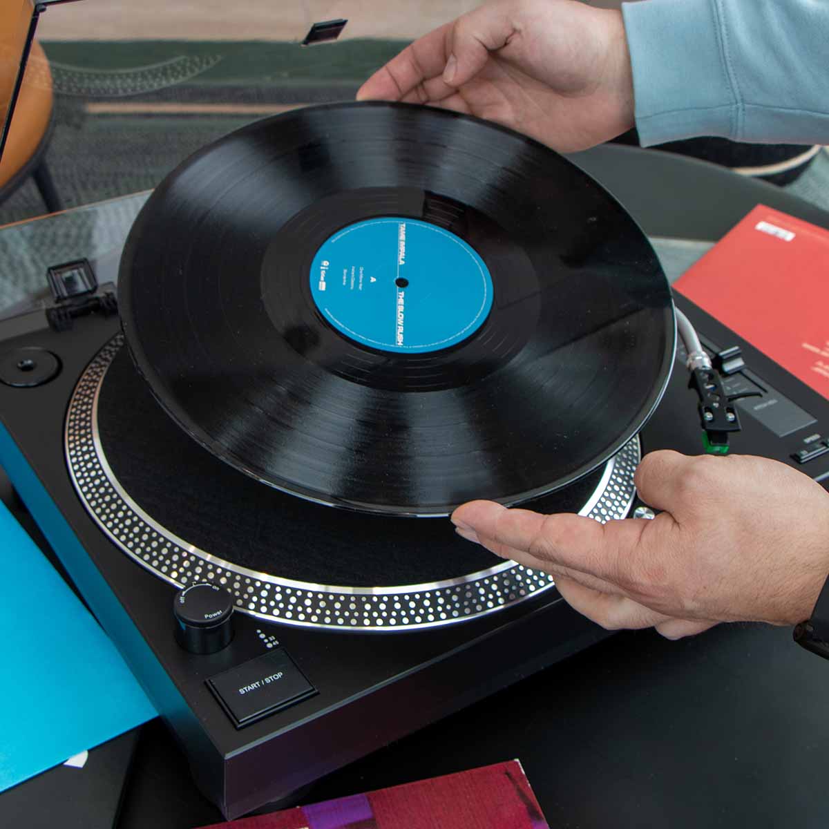 Lenco L-3828 Direct Drive Turntable high angle lifestyle shot with hands placing record on platter