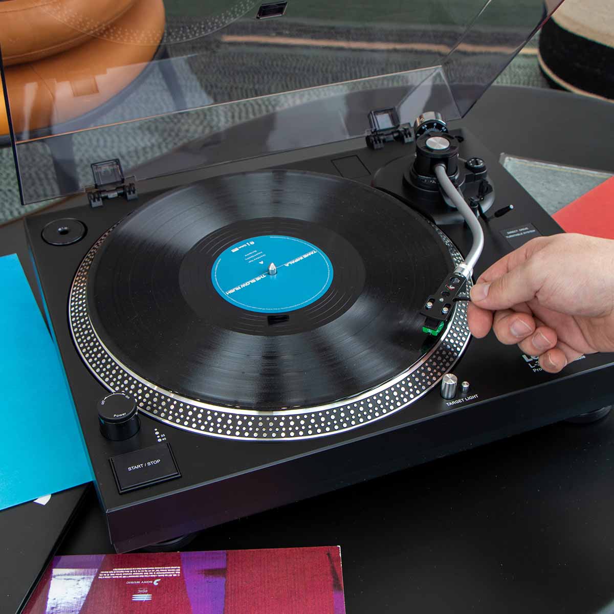Lenco L-3828 Direct Drive Turntable high angle lifestyle shot with record on platter and hand placing tonearm