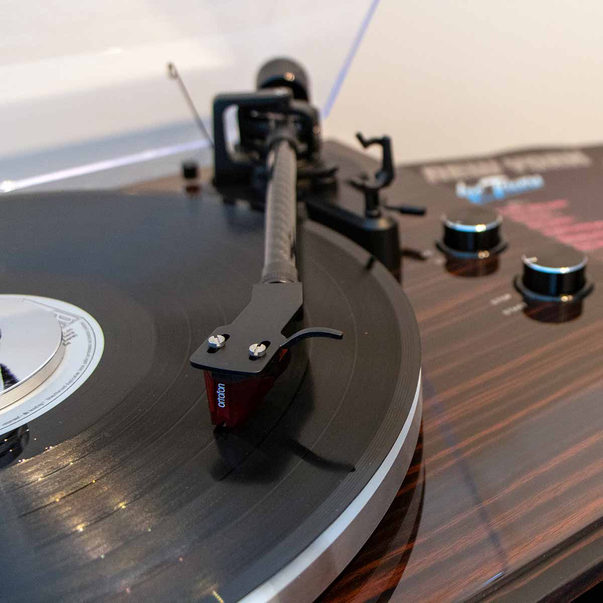 Lenco LBT-345 Bluetooth Turntable w/ Ortofon 2M Red lifestyle shot close-up of tonearm angled down and right with open dustcover and record on platter with tonearm engaged and record weight