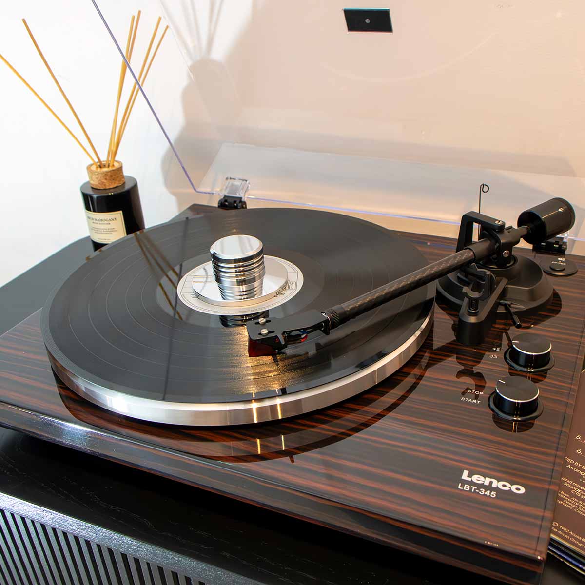 Lenco LBT-345 Bluetooth Turntable w/ Ortofon 2M Red lifestyle shot of unit on cabinet angled down and left with open dustcover and record on platter with tonearm engaged and record weight