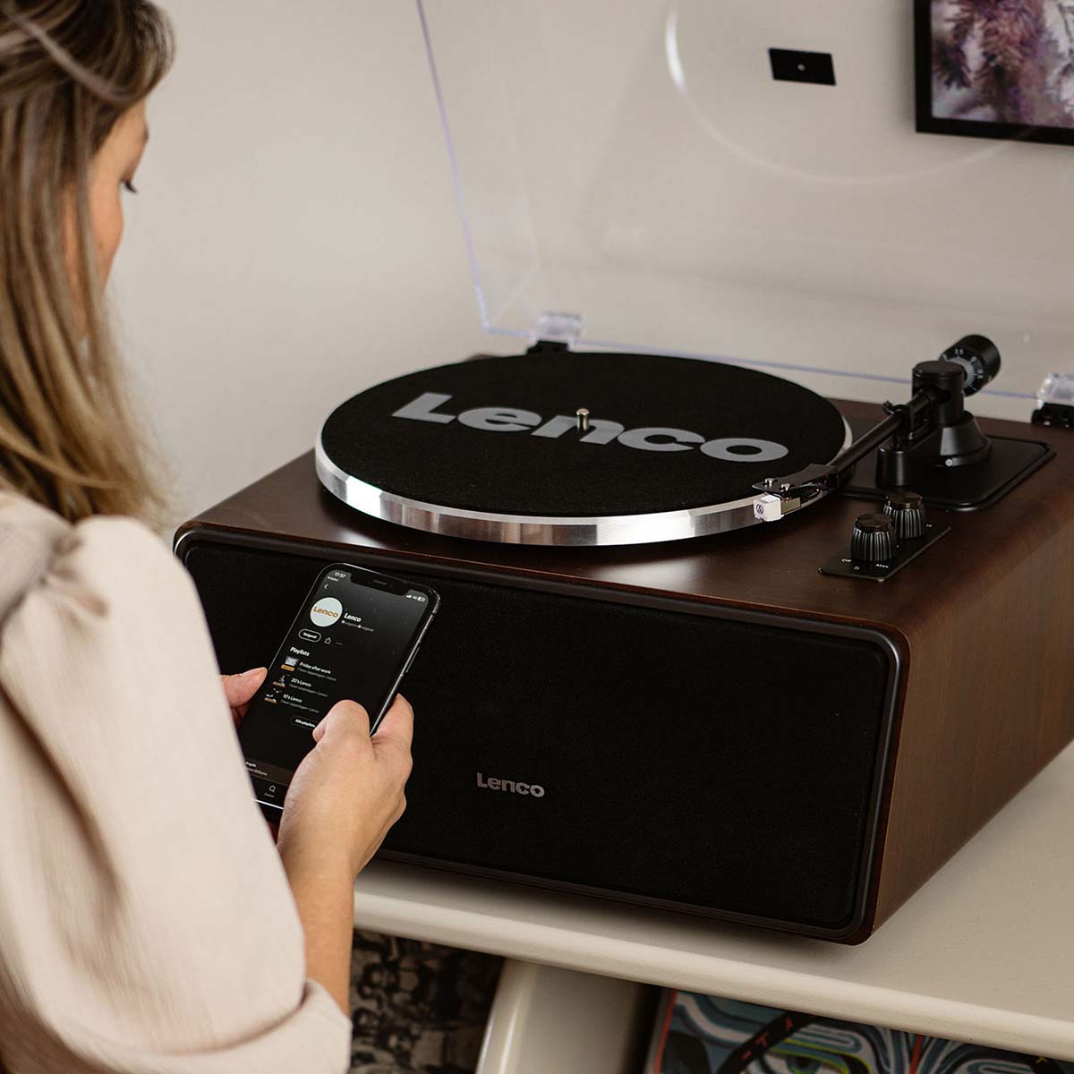 Lenco LS-470 Turntable w/ 80W Speaker System and Bluetooth lifestyle shot front view angled down with felt mat on platter and woman looking at phone
