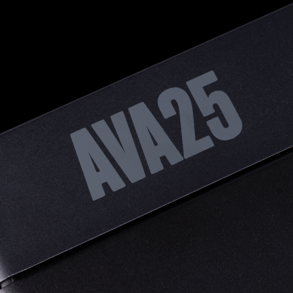 Close-up of a black rectangular product with large gray 'AVA25' lettering on a black background.