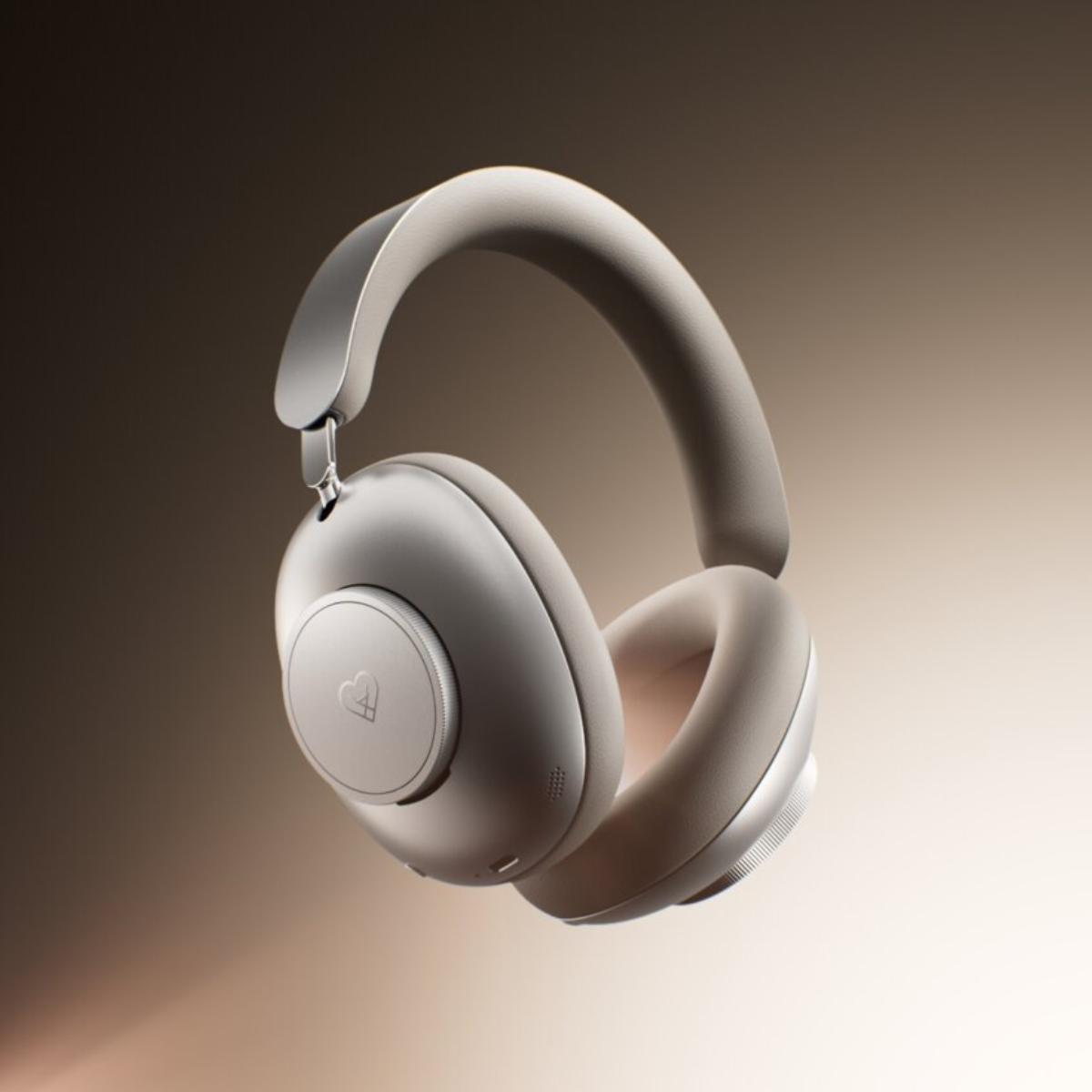 Over-ear wireless headphones in a matte light gray or off-white finish, shown floating against a warm brown-to-beige gradient background.