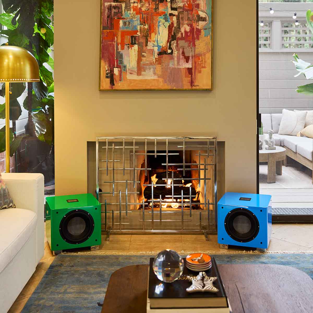 REL Acoustics T/9x SE Subwoofer Lifestyle photo of fireplace with green subwoofer to left and blue subwoofer to right both without grilles