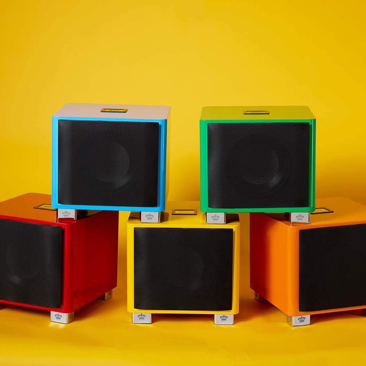 REL Acoustics T/9x SE Subwoofer pyramid of all five colors, blue and green stacked on red, yellow and orange all with grilles on yellow background