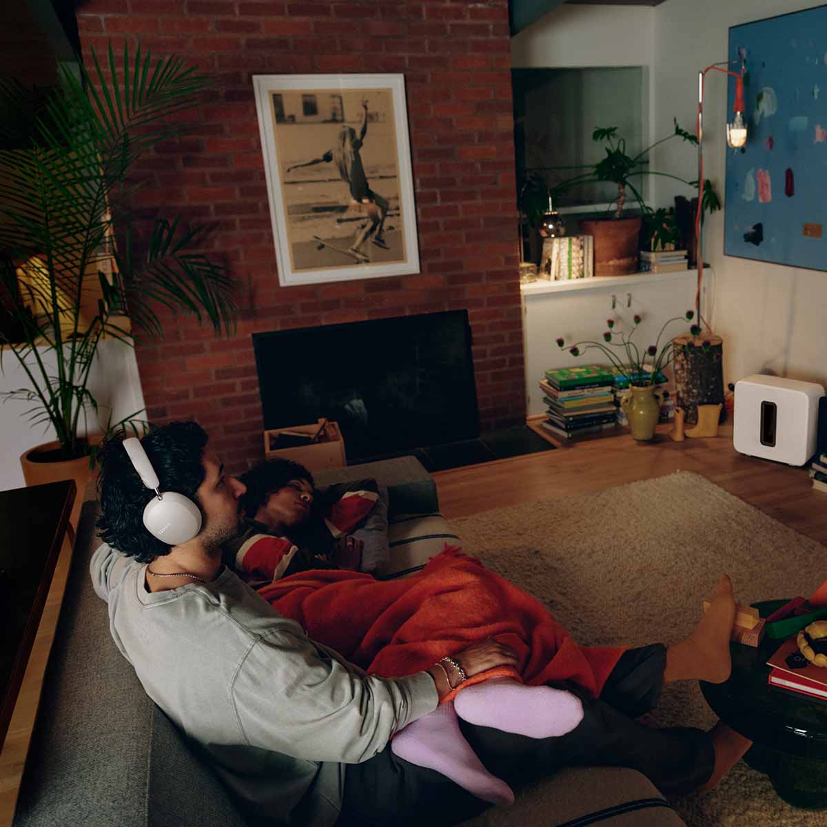 Sonos Ace Ultra Wireless Over-Ear Headphones - lifestyle photo of a couple sitting on a couch, one sleeps while the other wears white headphones