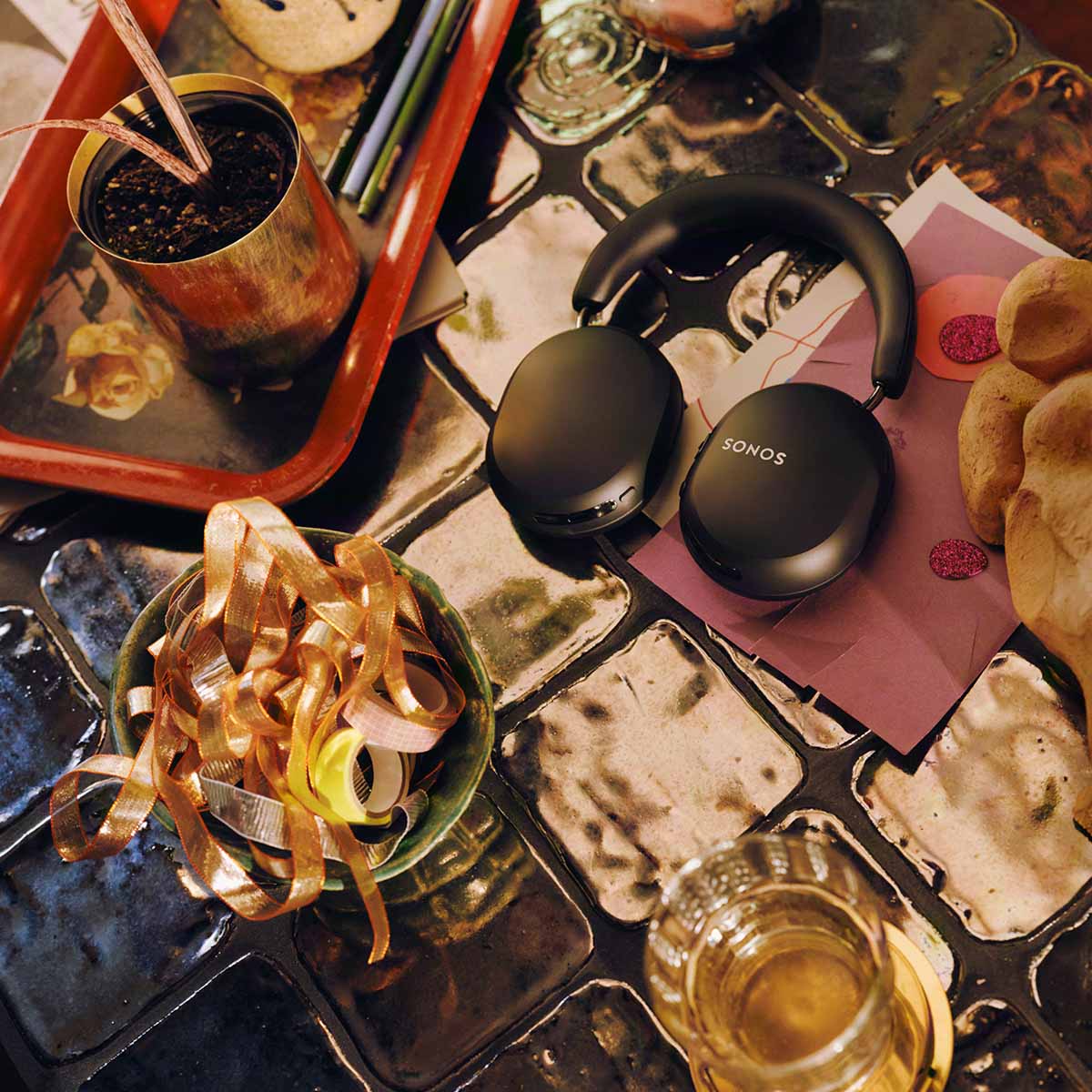 Sonos Ace Ultra Wireless Over-Ear Headphones - lifestyle photo of black headphones sitting on a cluttered tabletop