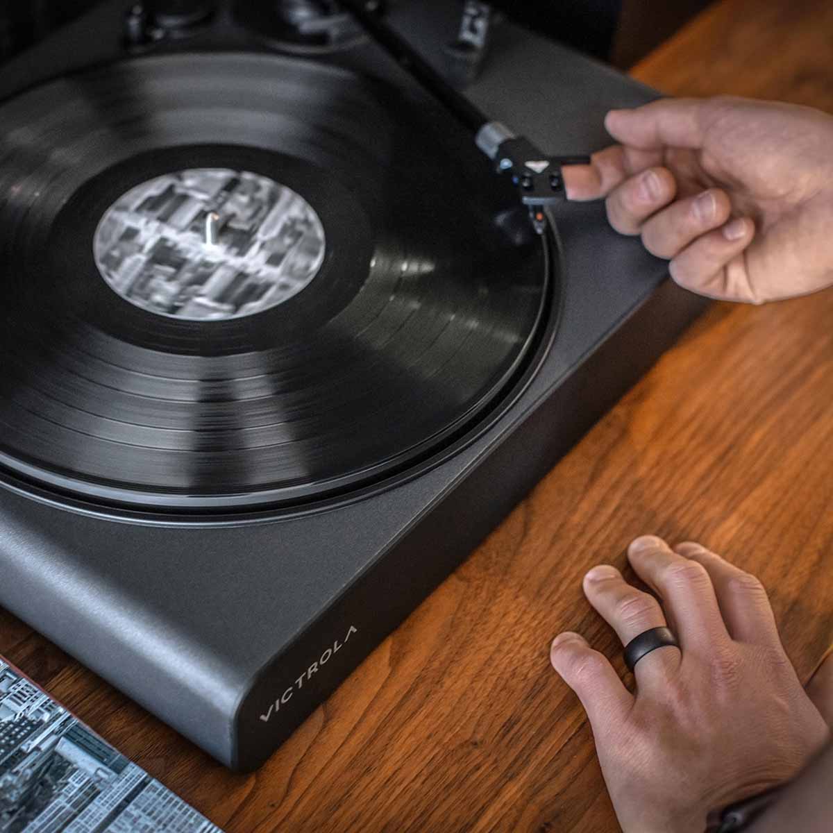 Victrola Stream Onyx Wi-Fi Streaming Turntable - Black - lifestyle view of unit on cabinet with hands placing needle on record
