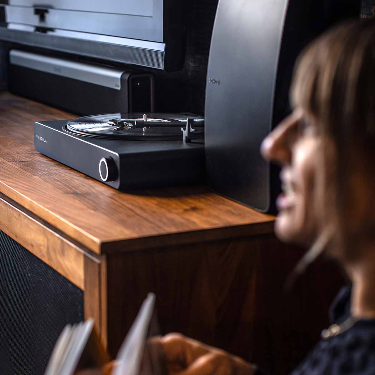 Victrola Stream Onyx Wi-Fi Streaming Turntable - Black - lifestyle view of unit on cabinet with woman out of focus in foreground