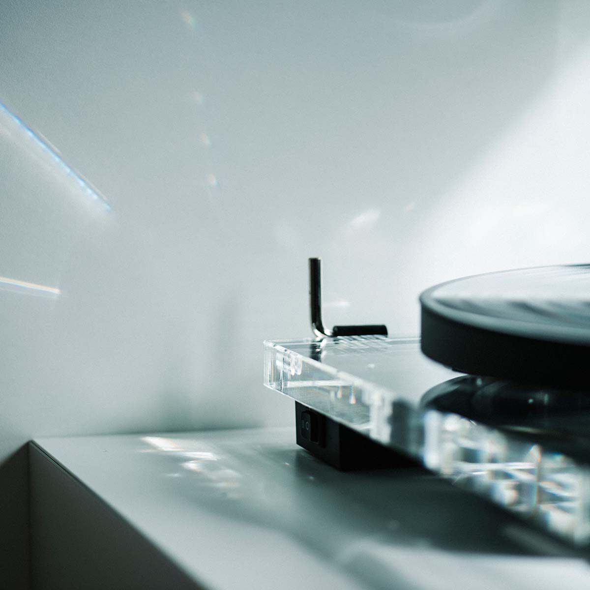 Pro-Ject XA B Balanced Acrylic Turntable - lifestyle shot low-angle detailed view of side of plinth and platter with record on platter and sunlight reflecting on back wall