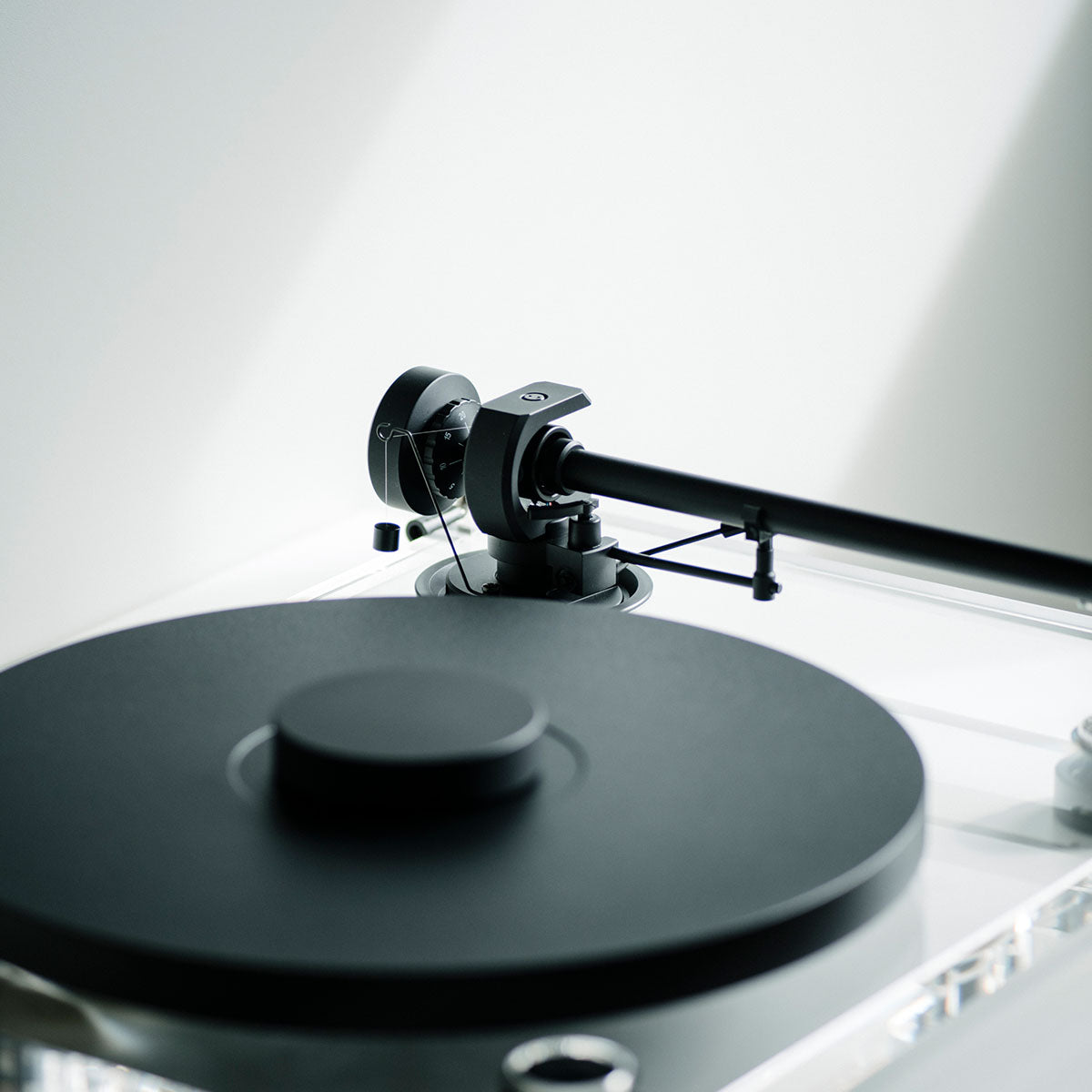 Pro-Ject XA B Balanced Acrylic Turntable - lifestyle shot detailed high-angle front view angled right of clear turntable on counter with sunlight reflected on back wall, puck on platter with no record and tone arm disengaged with focus on counterweight