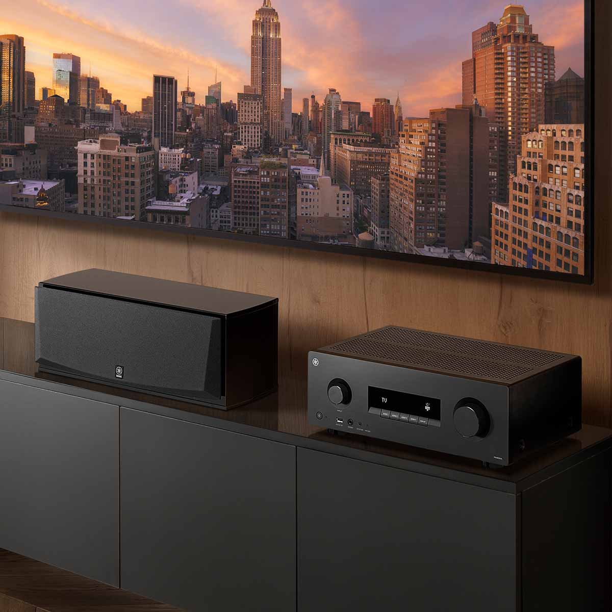 Yamaha RX500A 5.2-Channel AV Receiver - lifestyle image of unit on cabinet to right of speaker and below TV front view angled left
