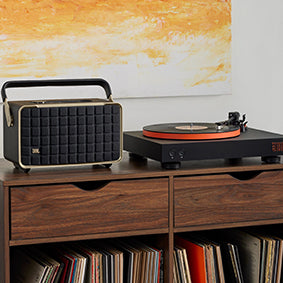 JBL Spinner BT Bluetooth Turntable in orange next to a retro speaker