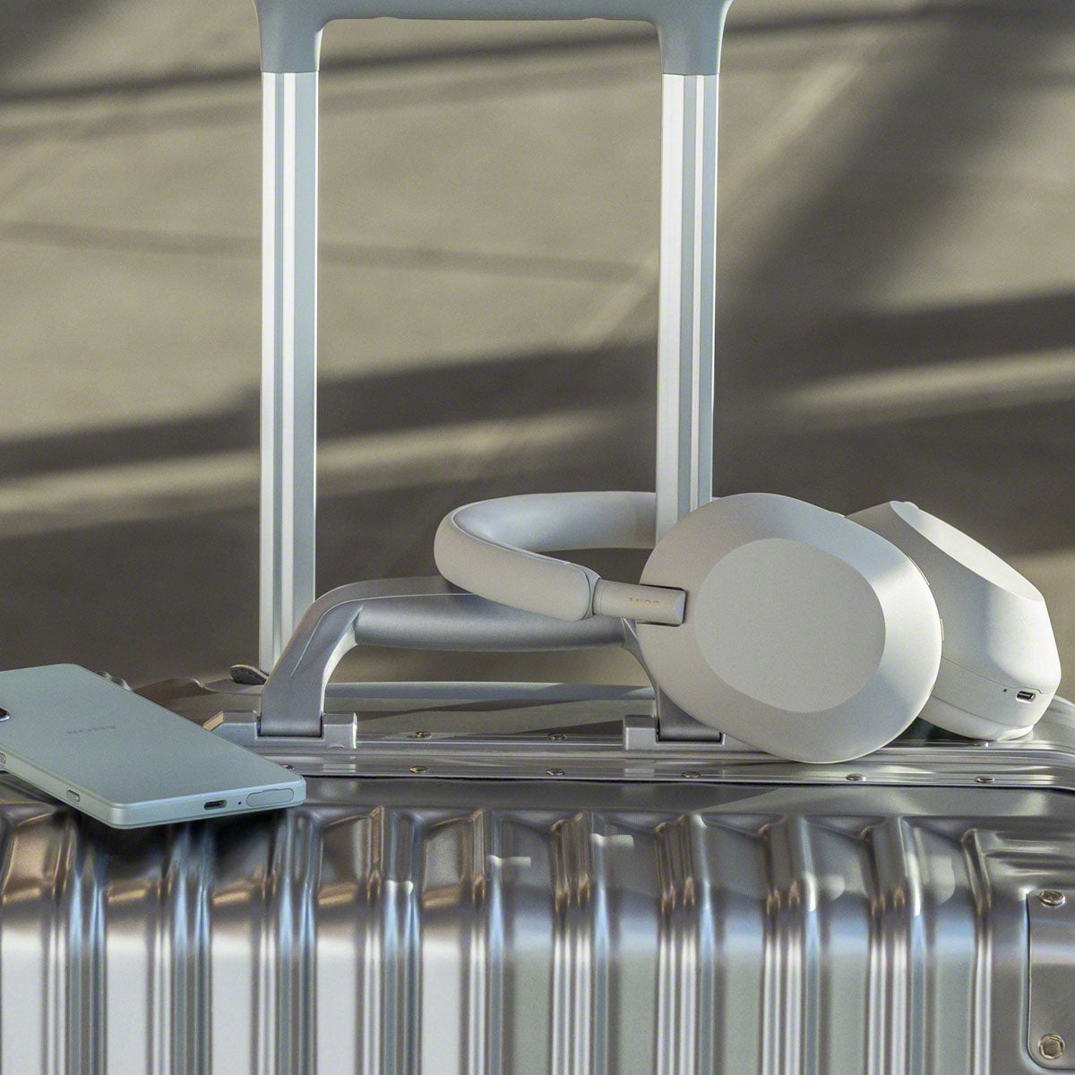 Lifestyle Image of Silver Sony WH-1000XM5 headphones sitting on a suitcase and beside a phone