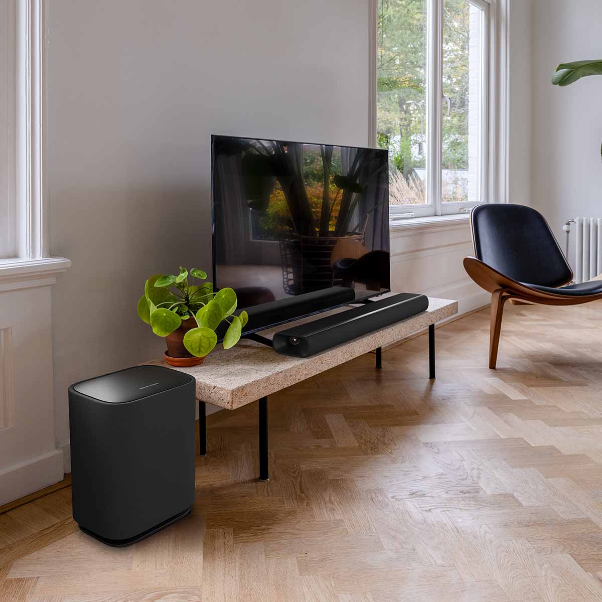 Harman Kardon Enchant Wireless Subwoofer lifestyle shot of sub to left of tv angled right