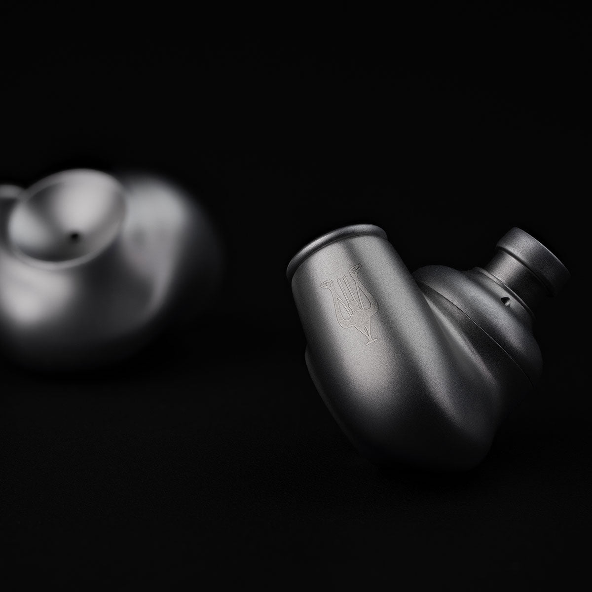 Meze Audio ASTRU Single Dynamic Driver In-Ear Monitors - artistic photo of both earbuds on black background, right earbud in focus showing Meze logo