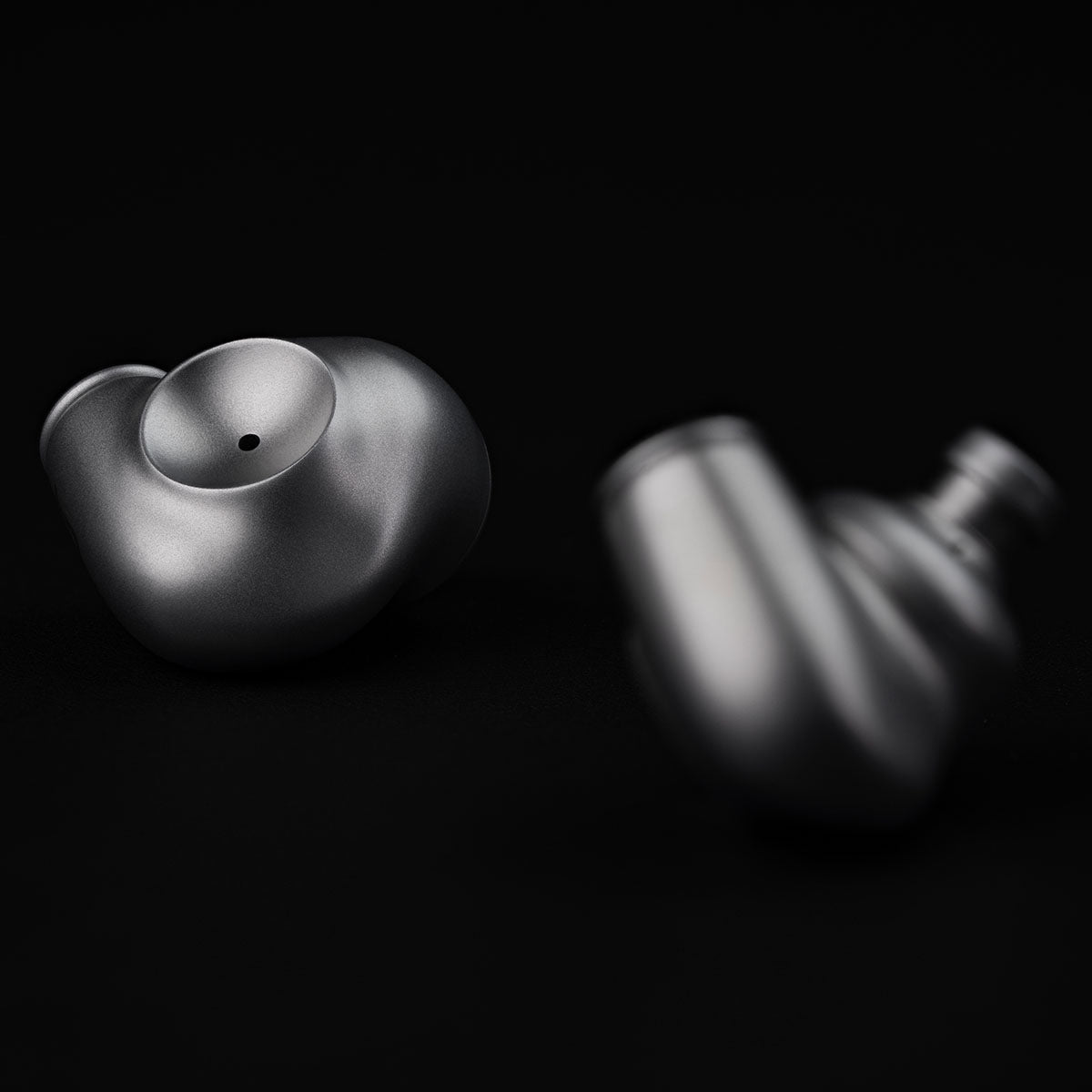 Meze Audio ASTRU Single Dynamic Driver In-Ear Monitors - artistic photo of both earbuds on black background, left earbud in focus