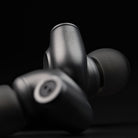 Meze Audio ASTRU Single Dynamic Driver In-Ear Monitors - artistic photo of both earbuds on black background, rear earbud in focus showing Meze logo