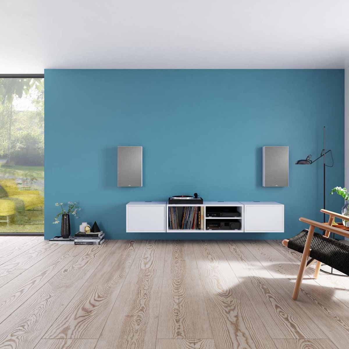 Lyngdorf FR-1 Speaker lifestyle shot front view pair of white units with gray grilles mounted on blue wall above white cabinet