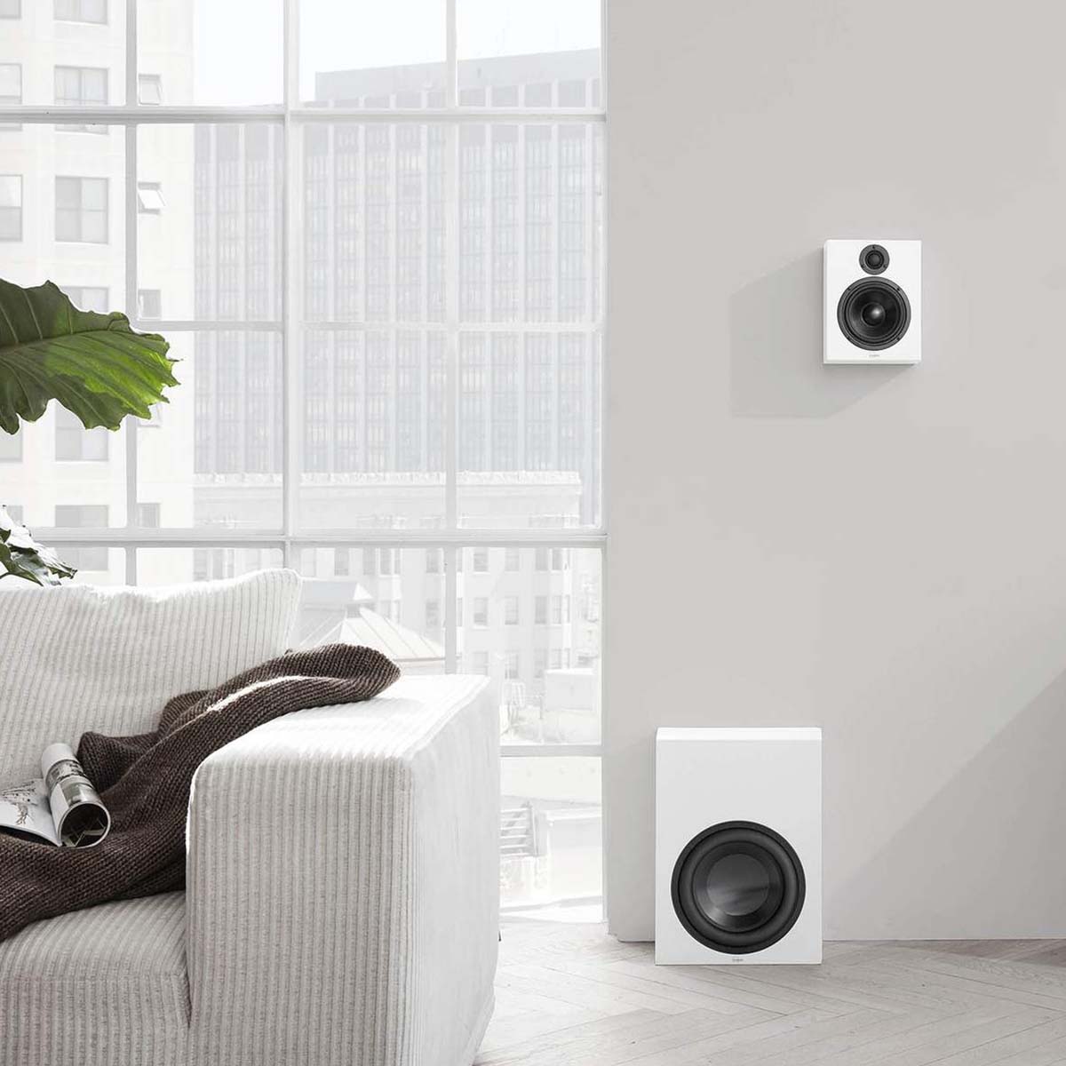 Lyngdorf BW-2 High Bandwidth Subwoofer white speaker without grille lifestyle view of speaker on floor with on-wall speaker above