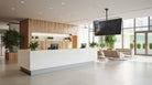 Modern office lobby with reception desk, chairs, and a large TV screen.