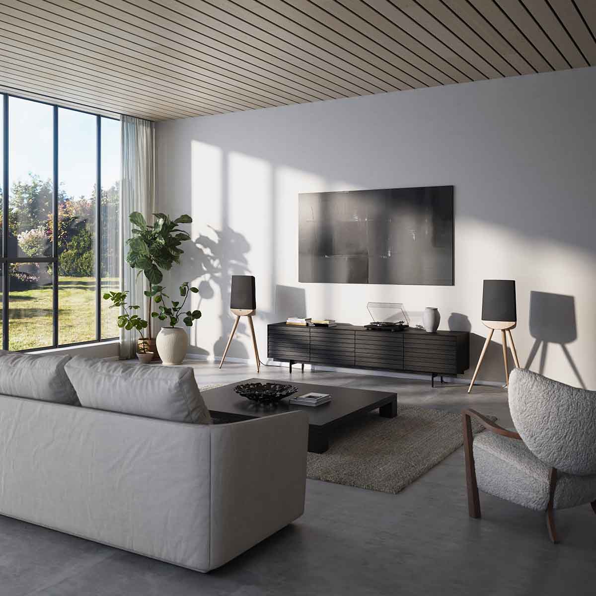 Lyngdorf Cue-100 Speaker lifestyle photo of speakers in living room, pair of speakers with oak base and black grilles