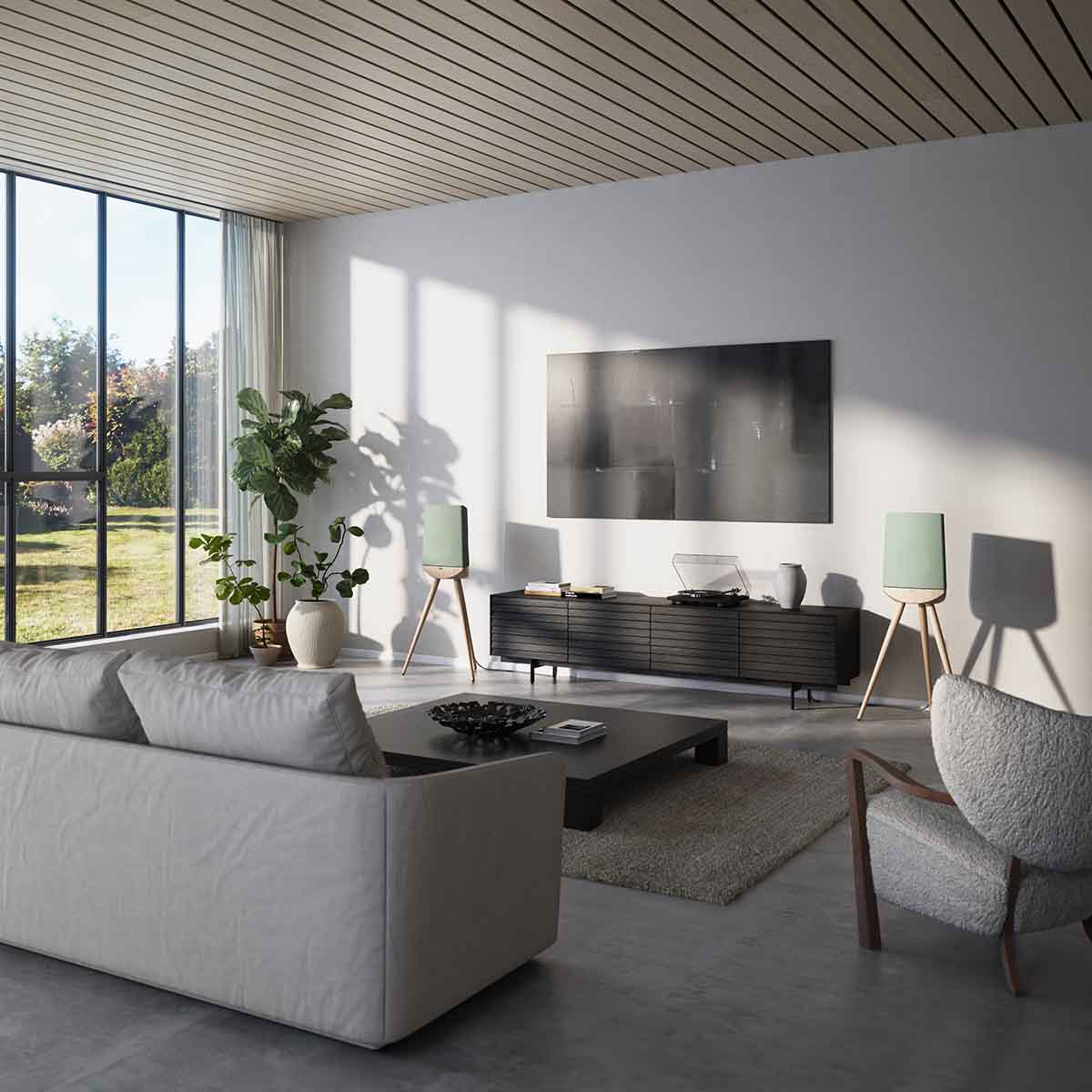 Lyngdorf Cue-100 Speaker lifestyle photo of speakers in living room, pair of speakers with oak base and green grilles