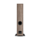 A single tall floor-standing speaker shown from the rear, featuring a wood-grain finish in a medium brown tone with a black circular driver and a small black brand badge near the base, set against a plain white background.
