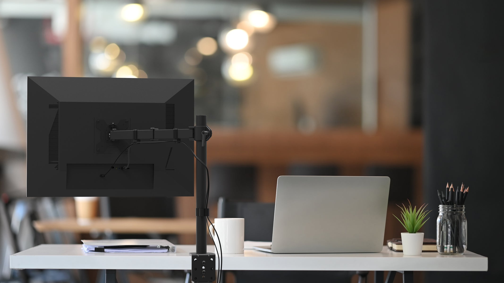 Black computer monitor on a stand with a laptop on a desk in a blurred office setting
