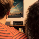 Denon AVR-S980H AV Receiver lifestyle photo of unit on cabinet with two people watching a movie in foreground
