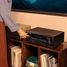 Denon AVR-S980H AV Receiver lifestyle photo of unit on cabinet with person adjusting knob