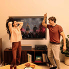 Denon AVR-S980H AV Receiver lifestyle photo of unit on cabinet with two people dancing in front of unit and tv