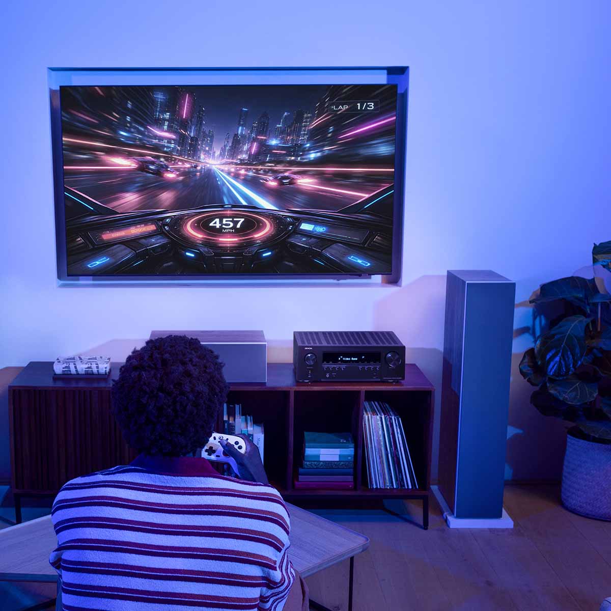 Denon AVR-S980H AV Receiver lifestyle photo of unit on cabinet under TV with person playing video games to front